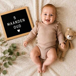 Baby van vijf maanden ligt op een zachte deken naast een knuffelbeertje en mijlpaalbord als herinnering aan de babytijd.